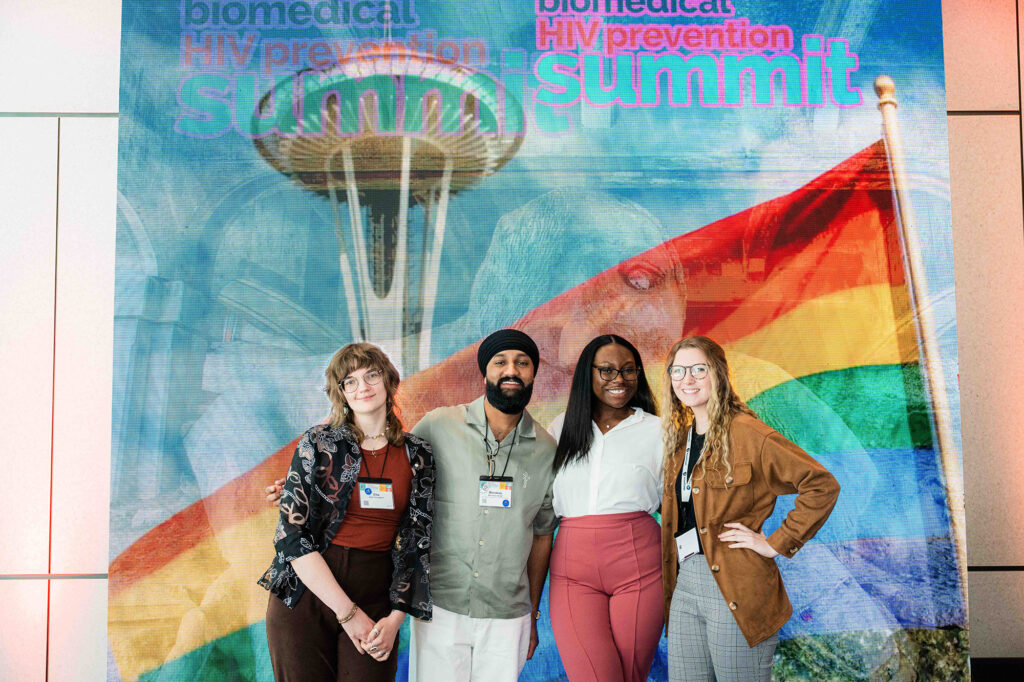 Four people pose in front of the Summit's conference banner.